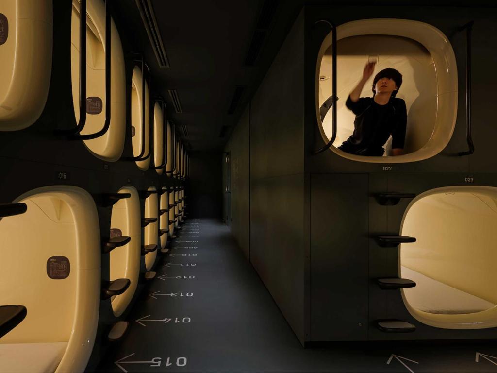 Two tiers of moulded sleeping capsules along a narrow lit corridor